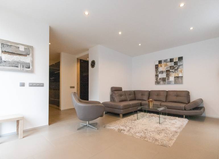 Exkluzívny 2i byt s terasou a parkovaním, Kramáre - Obývacia izba v 2-izbovom byte so sedačkou, kreslom, kobercom a obrazmi na stene.