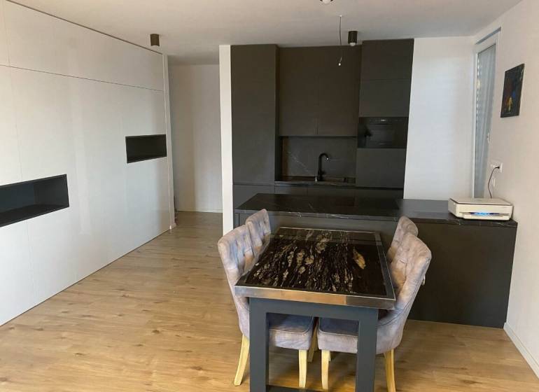 3-izb. byt, Zuzany Chalupovej, Petržalkou s veľkou terasou a saunou - Jedálenský kút s mramorovým stolom a kuchynskou linkou v 3-izbovom byte s podlahou s dreveným dekorom.