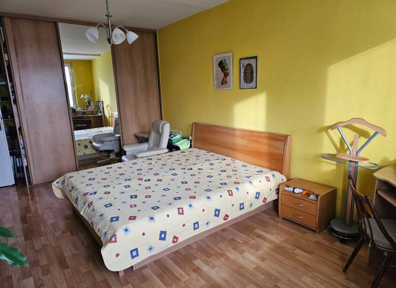 Veľký 2-izb. byt na ul. Nezábudková, Ružinov pri OC Retro - Spálňa v 2-izbovom byte s podlahou s dreveným dekorom, žltými stenami a vstavanou skriňou.
