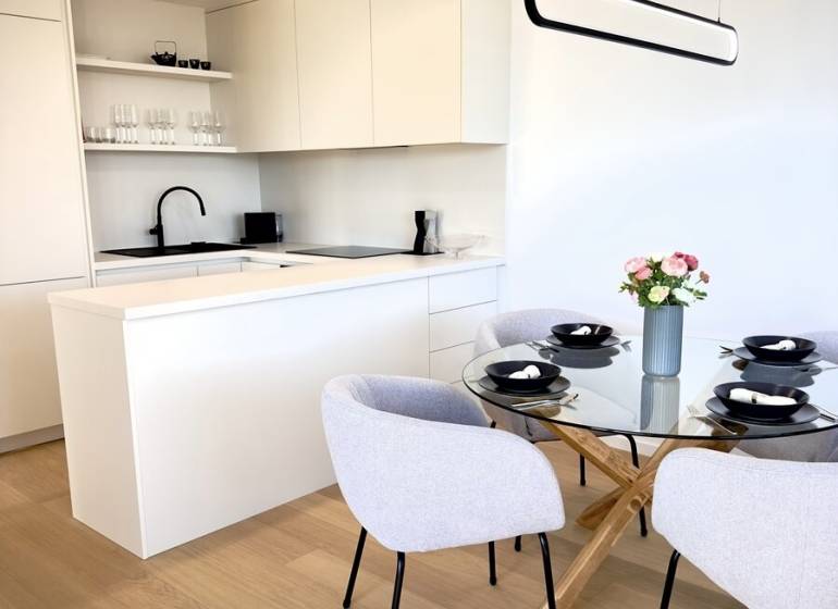 Prenájom 3-izbový byt s loggiou, SKY PARK, Bratislava - Kuchynský kút s bielymi skrinkami, skleneným stolom a podlahou s dreveným dekorom v 3-izbovom byte.