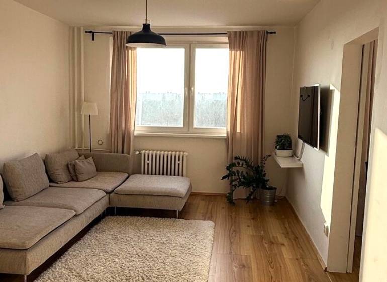 Prenájom pekný 3 izbový byt Jankolova ulica, Bratislava V. Petržalka - Obývacia izba v 3-izbovom byte s podlahou s dreveným dekorom a svetlou sedačkou.