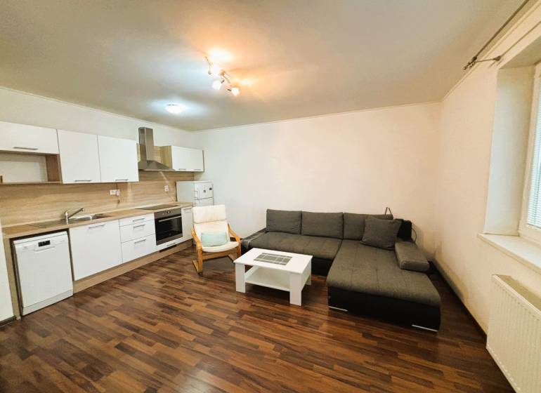 Prenájom 2 izbový byt – 52 m², lokalita – Malá Paka. - Obývacia izba v 2-izbovom byte s rohovo umiestnenou sedačkou a kuchynskou linkou.