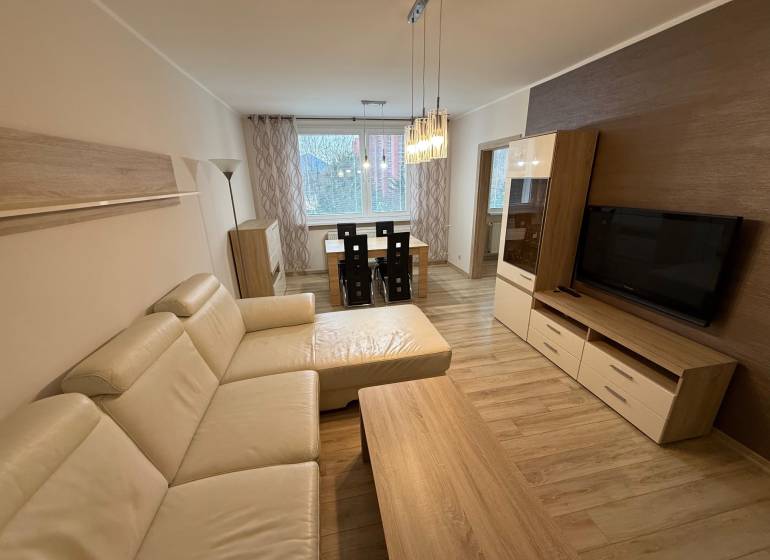 PRENÁJOM Trojizbový zariadený byt, Žilina - Vlčince - Obývacia izba s podlahou s dreveným dekorom, veľkou pohovkou a jedálenským stolom v 3-izbovom byte.