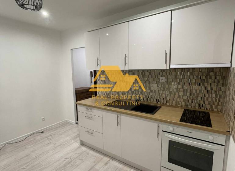 Prenajmem prerobený 1 izbový byt v Nových Zámkoch - Kuchyňa v 1-izbovom byte so svetlou linkou a podlahou s dreveným dekorom.