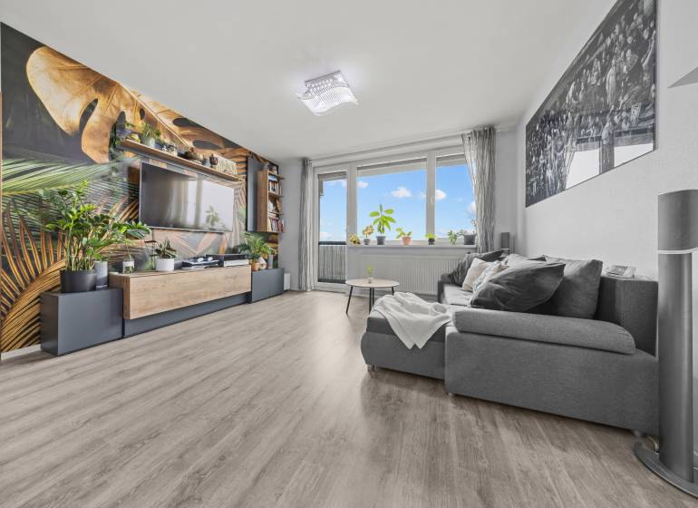 KOMPLETNE ZARIADENÝ 2-IZB. BYT,BALKÓN + PIVNICA,BUDATÍNSKA – PETRŽALKA - Obývacia izba s pohodlným gaučom, tapetou s rastlinným motívom a podlahou s dreveným dekorom.