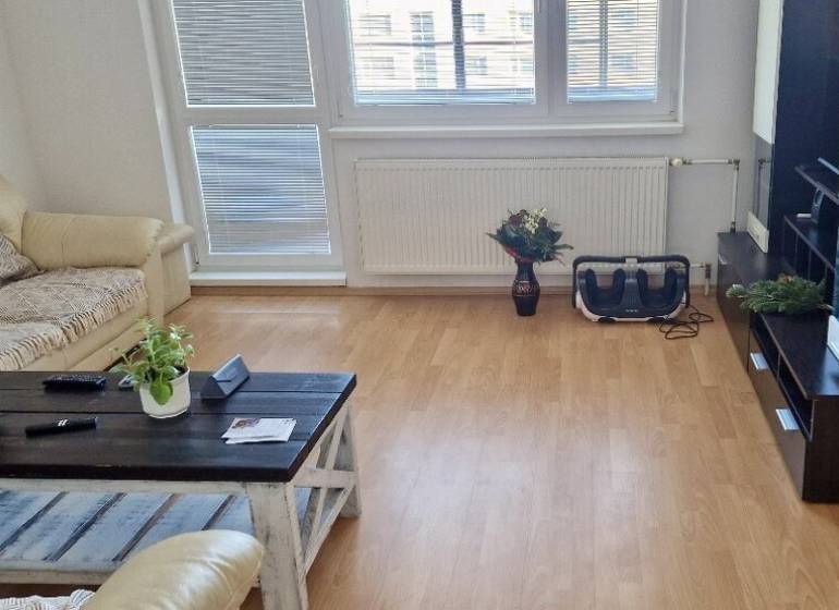 Prenájom 3 - izbový byt Bratislava - Petržalka - Obývacia izba v 3-izbovom byte s podlahou s dreveným dekorom a pohodlnou sedačkou.