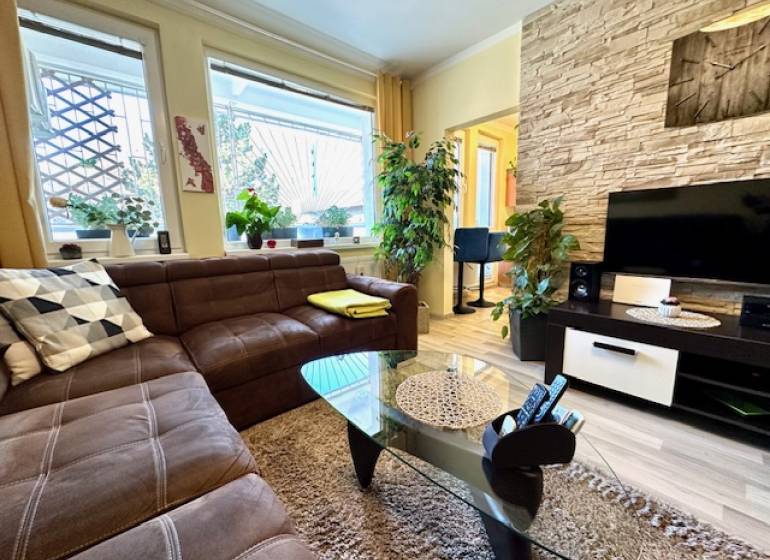 1 izb. zrekonštruovaný byt s veľkou loggiou, Karlova Ves - Obývačka v 1-izbovom byte s hnedou sedačkou a podlahou s dreveným dekorom.