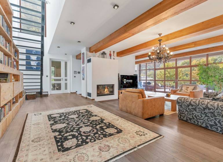 Nadštandardná 6-izbová vila v prominentnej lokalite - Interiér vily s krbom a knižnicou, doplnený o veľké okná a drevené trámy.