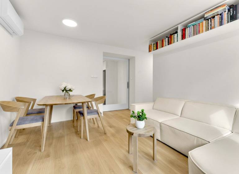 I Na predaj zrekonštruovaný 4i byt v Ružinove, Miletičova - Obývačka so svetlou sedačkou, stolom a podlahou s dreveným dekorom v 4-izbovom byte.