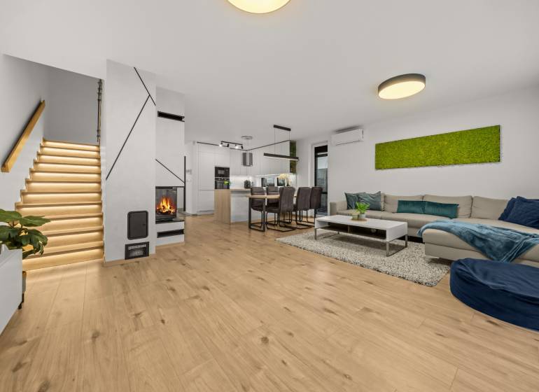 ROVINKA-Prenájom modernej, zariadenej novostavby 4 izbového rod.domu - Obývačka 4-izbového bytu s podlahou s dreveným dekorom, krbom a moderným schodiskom.