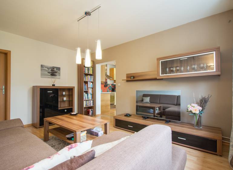 Pozrite si PRÍJEMNÝ 2i byt so ZARIADENÍM, LODŽIOU a KLIMATIZÁCIOU - Obývačka s podlahou s dreveným dekorom, pohovkou a policami v 2-izbovom byte.