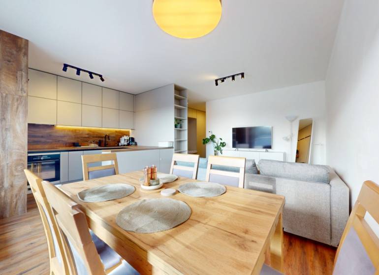 | Exkluzívny 4-izbový byt s obrovskou terasou | Stupava - Jasná kuchyňa s jedálňou a pohovkou v 4-izbovom byte, podlaha s dreveným dekorom.