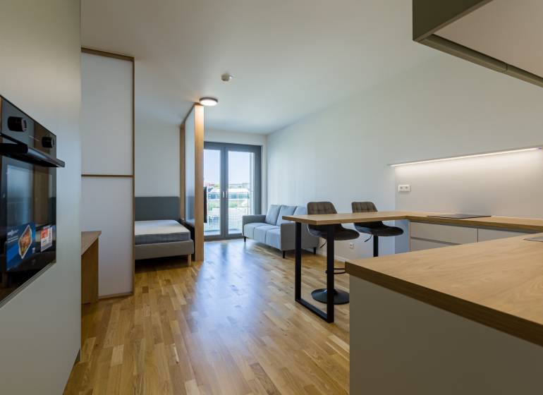 REZERVOVANÉ I METROPOLIS I Luxusný 1i byt I Staré Mesto - Interiér 1-izbového bytu s podlahou s dreveným dekorom, kuchynským ostrovčekom a sedačkou.