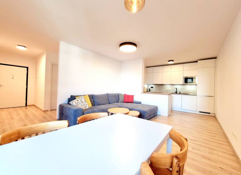 Pekný a moderný 3-izbový byt I Arboria Trnava - Obývačka v 3-izbovom byte s podlahou s dreveným dekorom, pohodlnou sedačkou a kuchynským kútom.