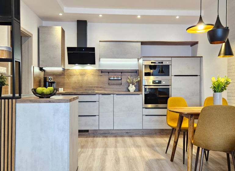 Moderný unikát - 1,5- izb. byt s 2 loggiami na prenájom (Nad jazerom) - Kuchyňa v 1-izbovom byte s podlahou s dreveným dekorom, jedálenský stôl a žlté stoličky.