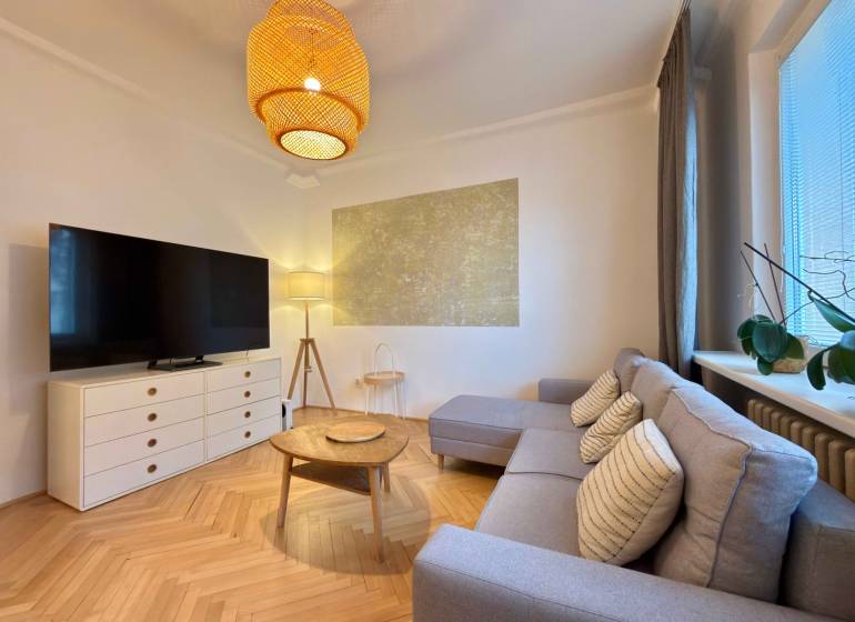 2-izbový byt 45m2 | Sklenárová - Ružinov - Obývačka v 2-izbovom byte s podlahou s dreveným dekorom, sedačkou a TV.