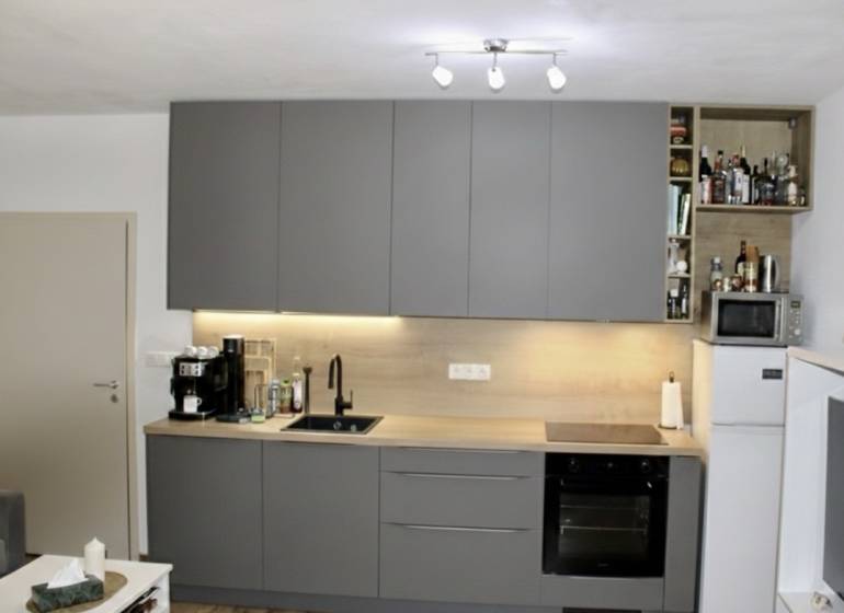 Prenájom 2-izb bytu Dlhé diely - Kuchyňa v 2-izbovom byte s tmavosivou linkou a spotrebičmi.