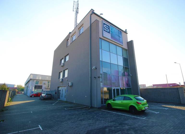 Predaj modernej administratívnej budovy v Bratislave, okres II - Budova so sklenou fasádou, parkoviskom a zelenej auto. Nachádza sa v priemyselnej oblasti.