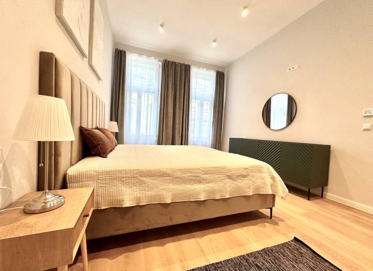 Prenájom priestranného 2-izbového bytu v absolútnom centre Košíc - Spálňa v 2-izbovom byte s veľkou posteľou, lampou a podlahou s dreveným dekorom.