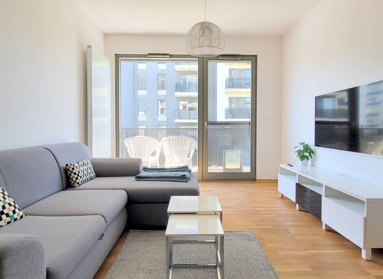 MODERNÝ 3i byt, CUBICON GARDENS, BALKÓN, PARKING, Rudolfa Mocka - Obývačka v 3-izbovom byte s pohovkou, podlahou s dreveným dekorom a terasou.