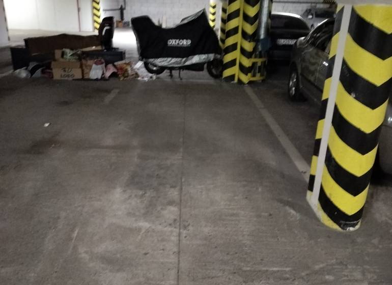 Garážové parkovacie miesto, NOVOSTAVBA, Krajná ulica, Trnávka - Parkovacie miesto v garáži s betónovou podlahou a vozidlom pod plachtou.