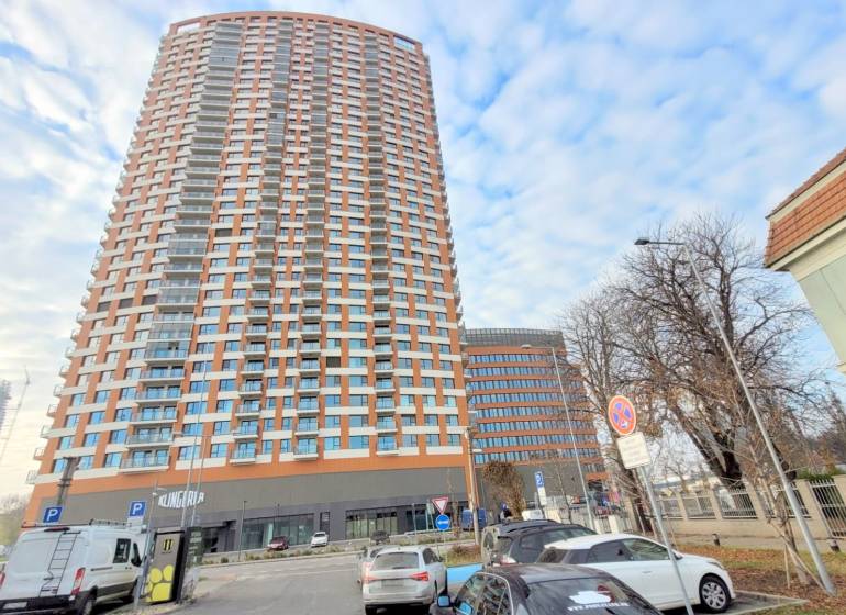 PRENÁJOM - VNÚTORNÉ PARKOVACIE STÁTIE, KLINGERKA, Súkennícka ulica - Veža v Bratislave - Ružinov na Súkenníckej ulici, obklopená autami a parkoviskom.