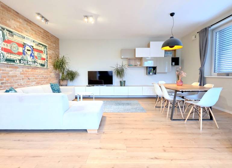 LUXUSNÝ 3i byt, TERASA, PARKING, KLÍMA, ZELENÁ HORKA, Ďumbierska ulica - Obývačka s bielym nábytkom, podlaha s dreveným dekorom, tehlová stena, obraz bankovky.