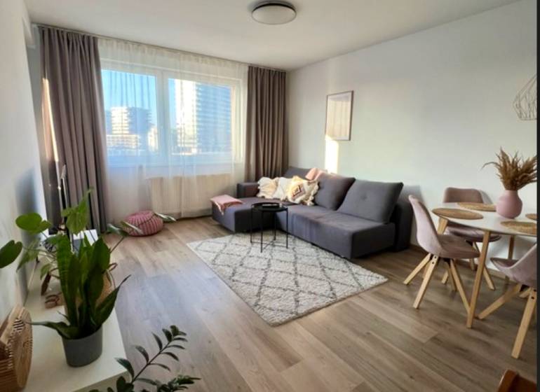 Novostavba FUXOVA 2 izbový byt, parking, Bosákova ul., BA V. Petržalka - Obývacia izba v 2-izbovom byte s pohovkou, stolom a podlahou s dreveným dekorom.