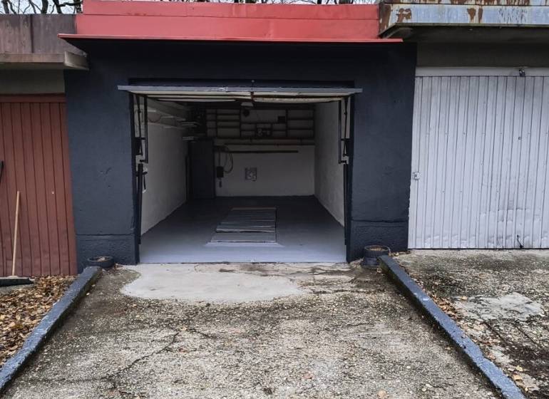 Garáž Púpavova, Karlova Ves + pivnica - Garáž na ulici Púpavová obklopená stromami, betónová dlažba a otvorené dvere.