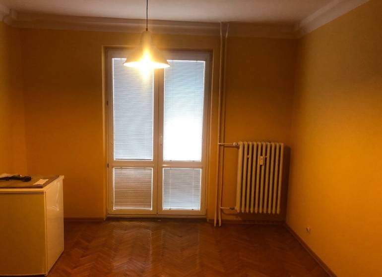 1-izb. byt na ul. Račianska, Nové Mesto s lodžiou - Žlté steny, podlaha s dreveným dekorom, radiátor a svetlo v 1-izbovom byte.