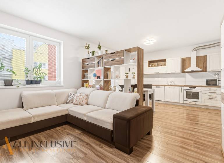 Na predaj moderný 2-izb. byt s loggiou vo Vrábľoch - Obývacia izba v 2-izbovom byte s veľkou sedačkou a kuchyňou, podlaha s dreveným dekorom.