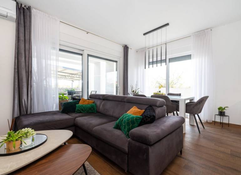 ZATON - Apartmán so záhradou - na predaj  - Obývacia izba v Rekreačnom apartmáne s pohovkou, podlahou s dreveným dekorom a jedálenským stolom.