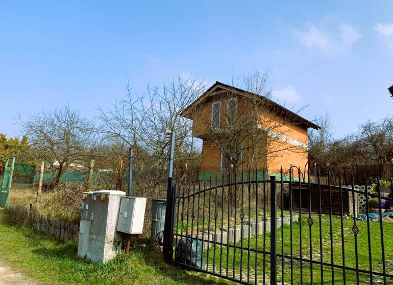 CHATA UZAVRETÁ HRUBÁ STAVBA, KOŠICKÁ NOVÁ VES - GEDER - Na obrázku je chata obklopená stromami a plotom na trávnatom pozemku.