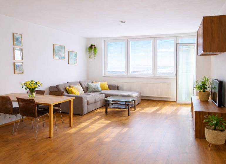 INVESTIČNÉ BÝVANIE V TOP LOKALITE: 2-IZBOVÝ BYT, JÉGÉHO UL, BRATISLAVA - Obývacia izba v 2-izbovom byte s rohovým gaučom a podlahou s dreveným dekorom.