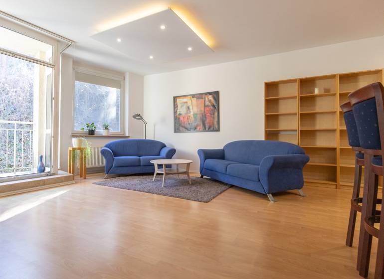 Priestranný 3-izbový byt s loggiou, Staré Mesto - Obývacia izba v 3-izbovom byte s modrými sedačkami a podlahou s dreveným dekorom.