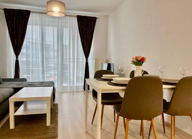 PRENÁJOM NOVOSTAVBA 2 izb.byt, BALKÓN, PARKOVACIE MIESTO, BIELY KOSTOL - 2-izbový byt s podlahou s dreveným dekorom, jedálenským stolom a pohovkou.