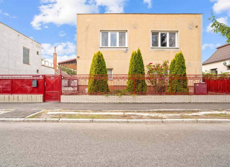 NA PREDAJ VÝNIMOČNÝ RODINNÝ DOM VO VEĽKOM MEDERI - Rodinný dom vo Veľkom Mederi so žltou fasádou, červeným plotom a zeleňou pred domom.