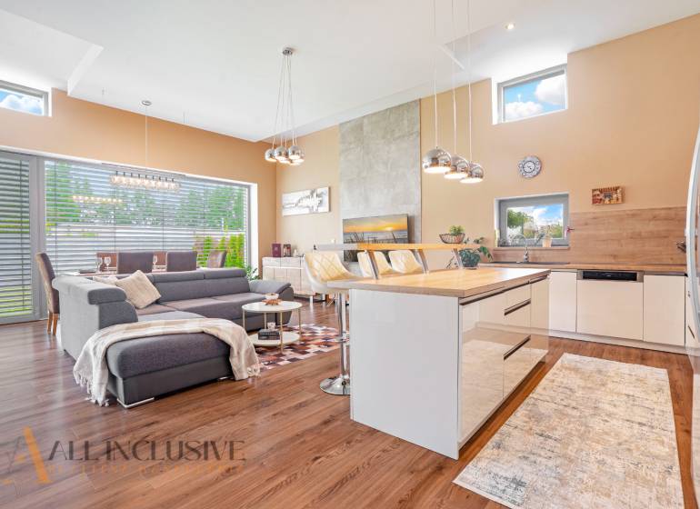 NA PREDAJ NADŠTANDARDNÁ 4-IZB. NOVOSTAVBA, DUN. KLÁTOV - Obývačka v rodinnom dome s kuchyňou, sivou sedačkou a jedálenským stolom.