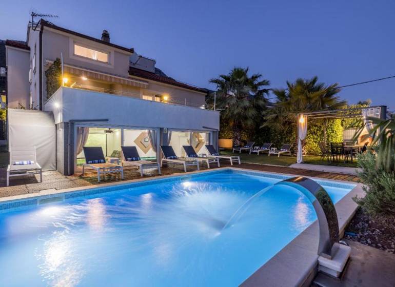 Kaštela(HR)-moderná vila s krásnym výhľadom - Vila v Kaštela s osvetleným bazénom, ležadlami a palmami v záhrade pri súmraku.