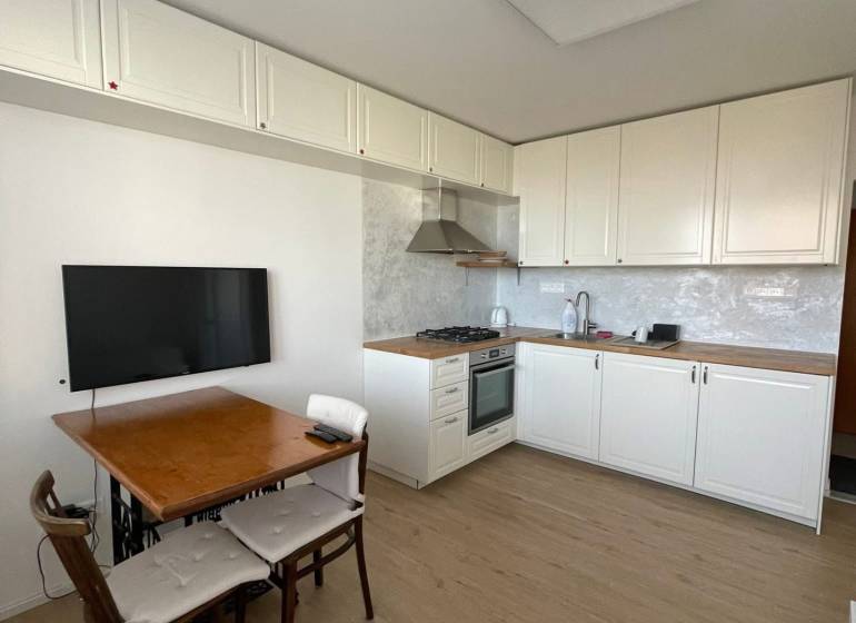 Prenajmem 1 izbový byt na Nábrežnej ulici v Nových Zámkoch - Kuchyňa v 1-izbovom byte s podlahou s dreveným dekorom a jedálenským stolom.