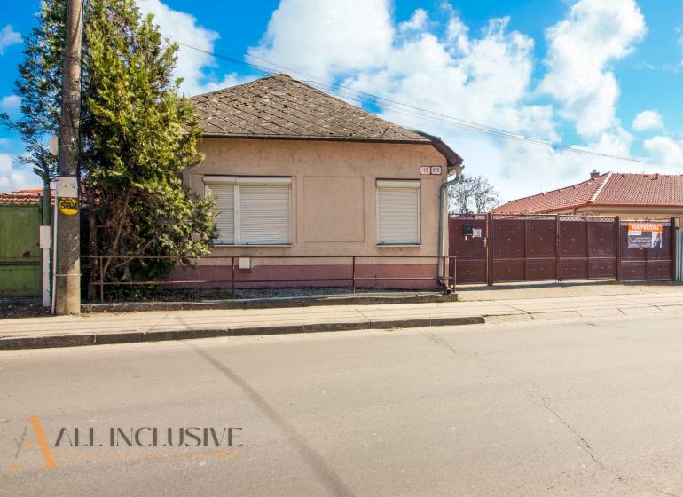 NA PREDAJ 4-IZBOVÝ RODINNÝ DOM NA PRIESTRANNOM POZEMKU - Rodinný dom s plotom, stromom a výveskou na predaj, vhodný na bývanie.