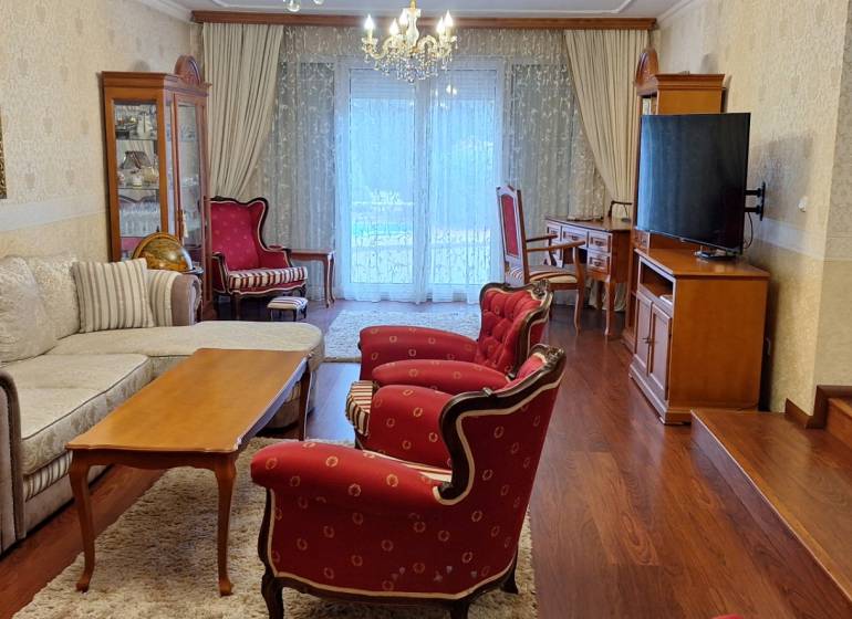 Luxusný rodinný dom s bazénom a dvojgarážou v Komárne - Obývacia izba v rodinnom dome s červenými kreslami a podlahou s dreveným dekorom.