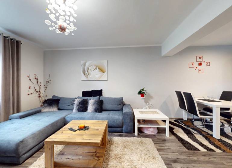 Prerobený rodinný dom na veľkom tichom pozemku v obci Pruské   - Obývačka v rodinnom dome s modrou sedačkou, jedálenským stolom a podlahou s dreveným dekorom.