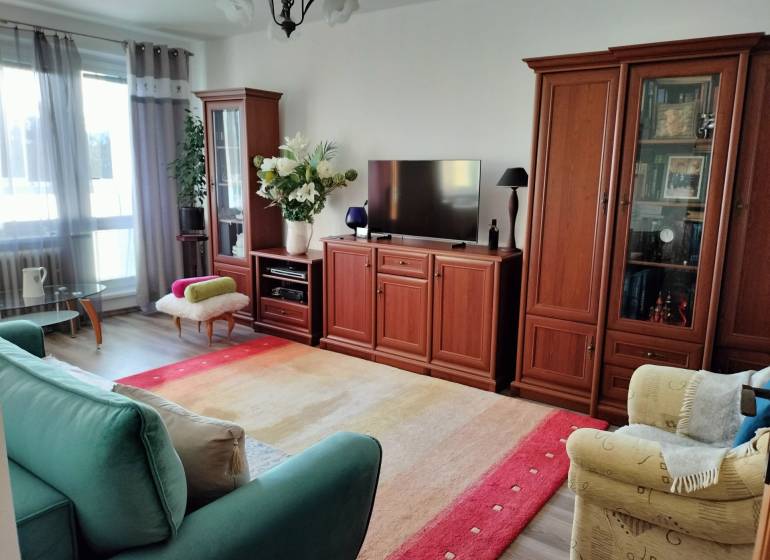 2 izbový byt na Severe - Obývacia izba v 2-izbovom byte s podlahou s dreveným dekorom a pohodlným nábytkom.