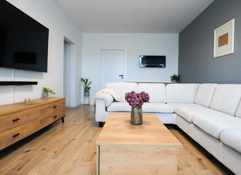 Rezervované -  3i byt v Nemšovej s loggiou po rekonštrukcii - 74m²  - Obývačka v 3-izbovom byte s bielym gaučom, podlahou s dreveným dekorom a dekoráciami.