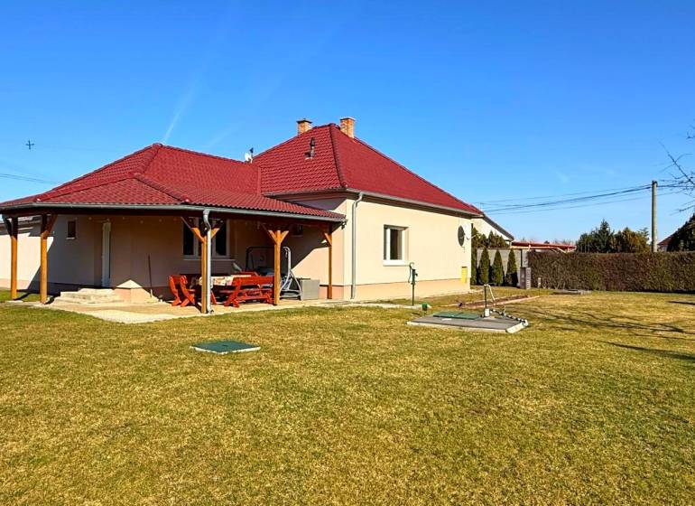 ZĽAVA!! NA PREDAJ RODINNÝ DOM V ZEMIANSKEJ OLČI – PO REKONŠTRUKCII - Rodinný dom v Zemianskej Olči s červenou strechou a dreveným prístreškom, trávnatá záhrada.
