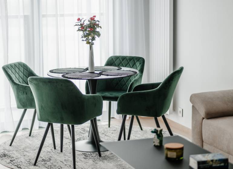 | E2Tower | 20.poschodie | 2i byt | panoramatický výhľad |  - Zelené kreslá a stôl s kvetom v 2-izbovom byte na podlahe s dreveným dekorom.