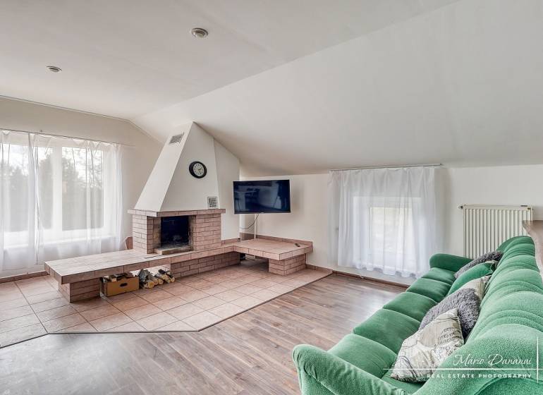 4-izbový podkrovný byt s nebytovým priestorom v obci Pavlice - Obývačka s krbom, zelenou pohovkou a podlahou s dreveným dekorom v rodinnom dome.