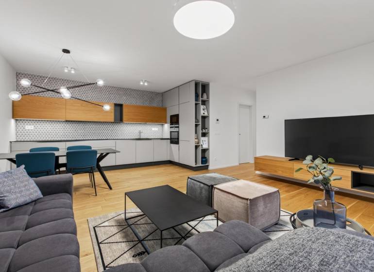 ︱ PREDAJ Nadštandardný 3-izb. byt v projekte Gansberg Koliba - Obývacia izba s kuchyňou v 3-izbovom byte, podlaha s dreveným dekorom, moderný nábytok.