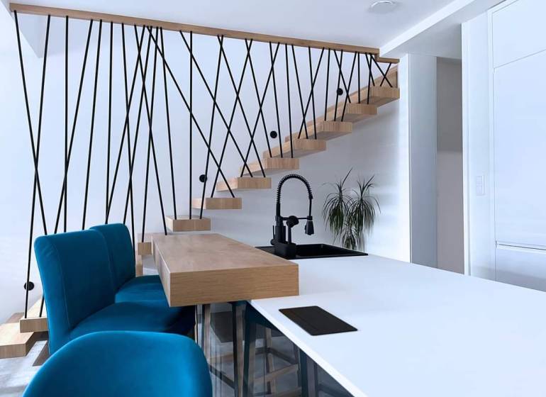 Poschodový rodinný dom v Michalovciach  - Interiér rodinného domu so schodiskom, modrými stoličkami a kuchynským pultom.